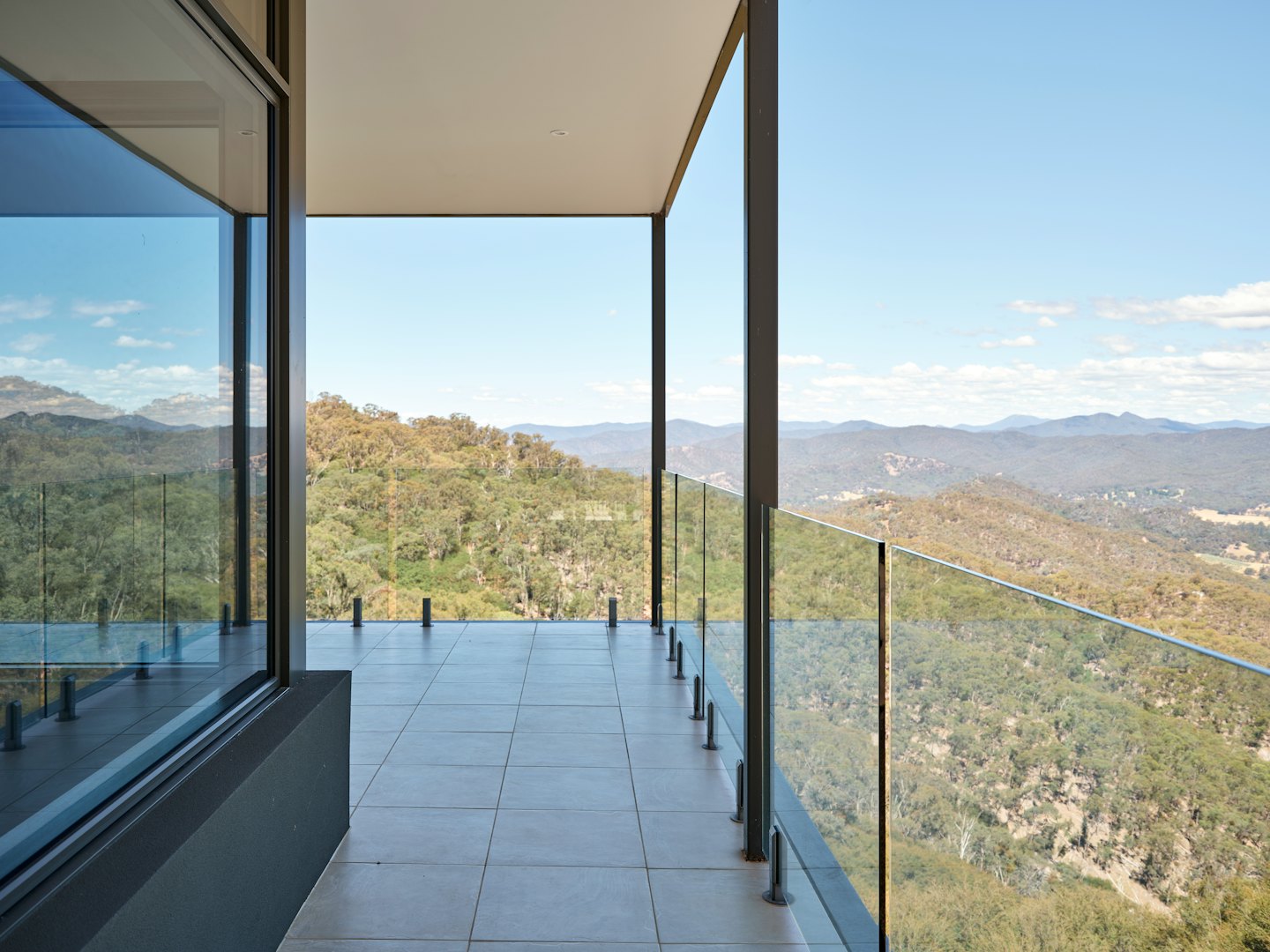 Modern balcony overlooking a vast forested mountain landscape.